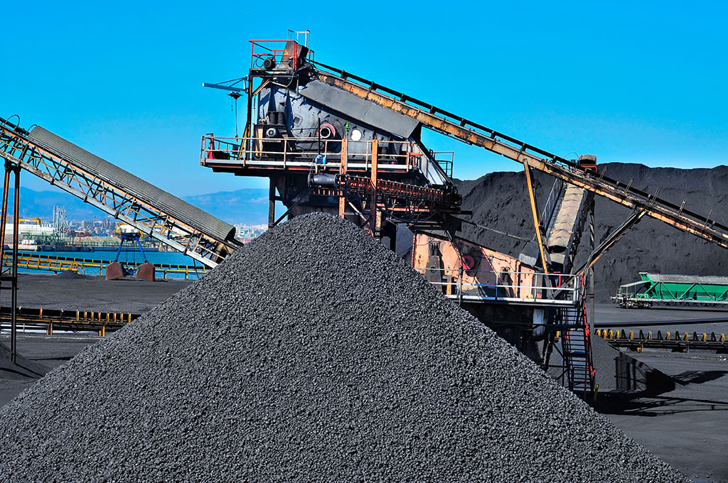 blue sky contrasted against a coal mine conveyor with a mountain of dark coal