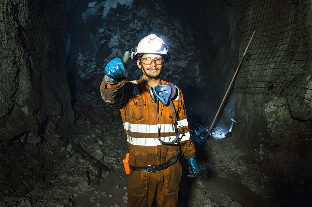 Miner in the mine. Well-uniformed miner inside mine raising thumb for mining safety